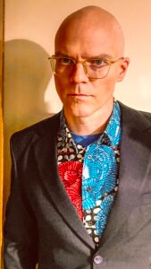 A bald man in glasses looks into the camera